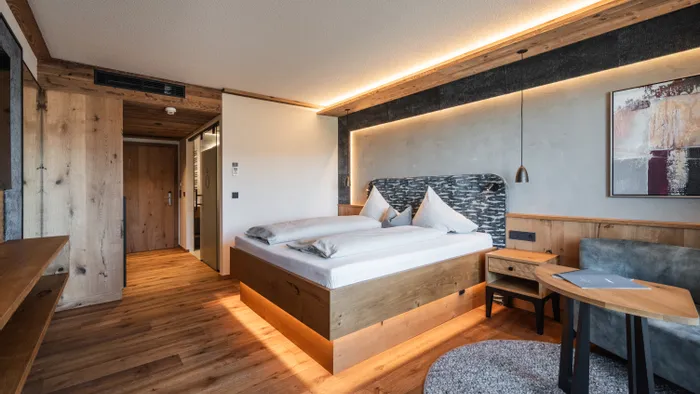 Modern hotel room with wooden furnishings, double bed, accent lighting, and cozy seating area