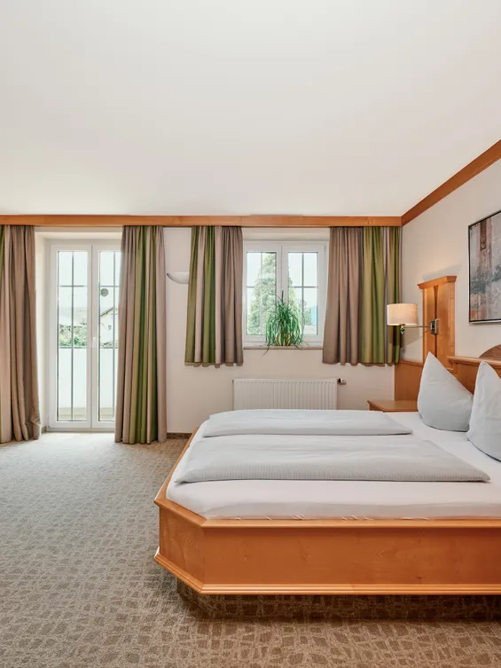Geräumiges Hotelzimmer mit Doppelbett, Holzmöbeln, Schreibtisch und Tageslicht vom Balkon