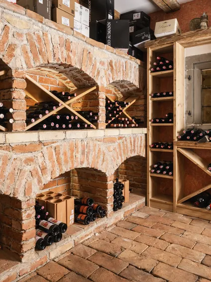 Cantina rustica con scaffali in mattoni e portabottiglie in legno pieni di bottiglie di vino rosso