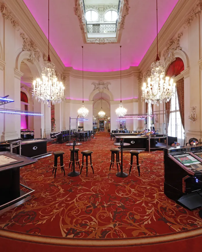Elegant casino interior with slot machines, gaming tables, chandeliers, and red carpet decor