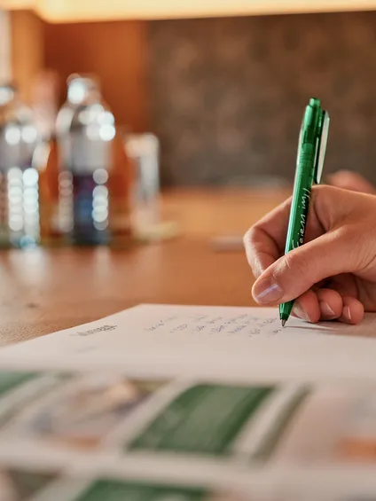 Hand schreibt Notizen mit grünem Stift während eines Geschäftstreffens im Konferenzraum