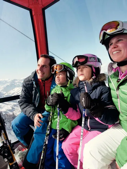 Family in ski gear riding gondola lift with snowy mountains in the background