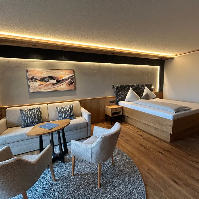 Modernes Hotelzimmer mit Holzboden, Doppelbett, Sofa, Sesseln und stimmungsvoller Beleuchtung