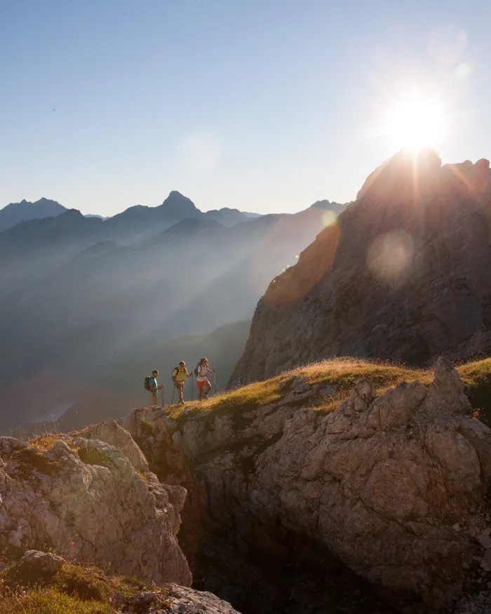 Escursionisti su sentiero di montagna all'alba con vette rocciose nelle Alpi