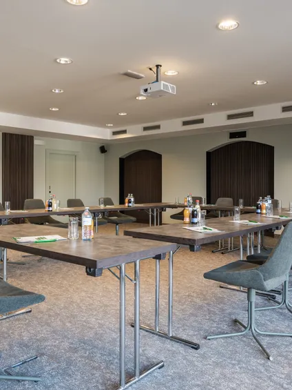 Moderner Konferenzraum mit U-förmiger Tischanordnung, Stühlen und Getränken für ein Geschäftstreffen