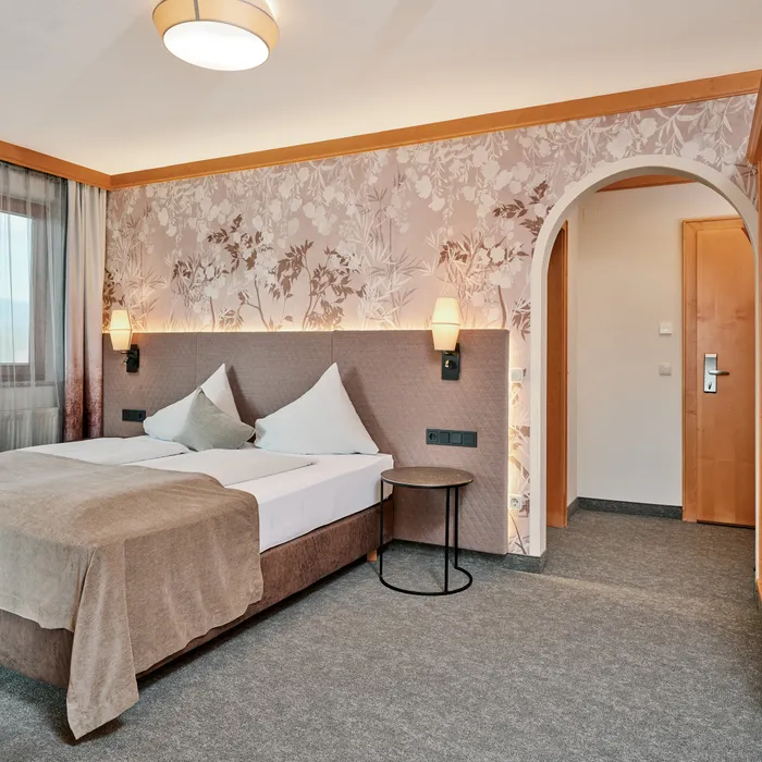 Gemütliches Hotelzimmer mit Doppelbett, Blumenmuster-Tapete und sanfter Beleuchtung