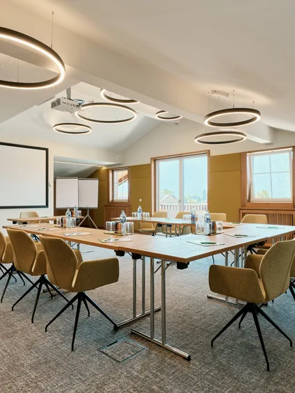 Moderner Konferenzraum mit U-förmigem Tisch, Beamerleinwand und runden Deckenleuchten