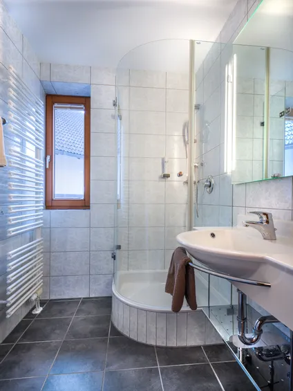 Modernes kleines Badezimmer mit Eckdusche, weißem Waschbecken, Handtuch und gefliesten Wänden und Boden