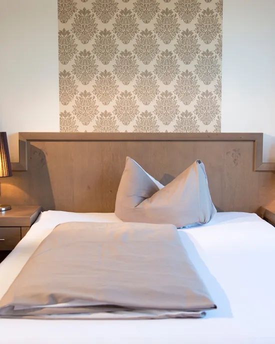 Modernes Hotelzimmer mit Holz-Doppelbett, Nachttischlampen und eleganter Tapete