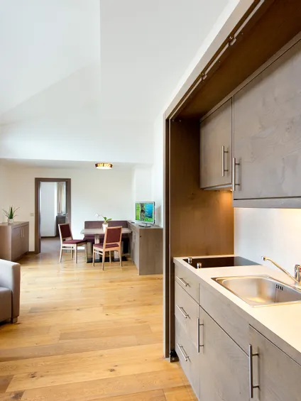 Moderne Hotelsuite mit Kochnische, Essbereich, Sesseln und großen Fenstern