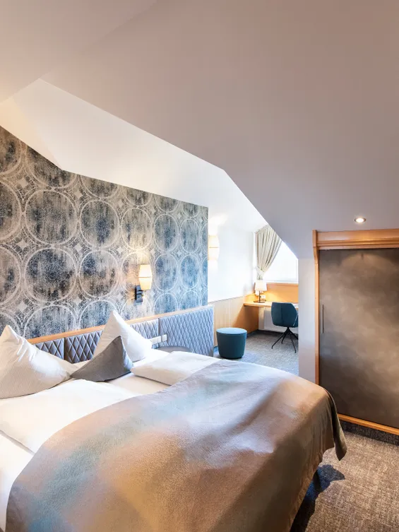 Modernes Hotelzimmer mit Doppelbett, gemusterter Wand, Schreibtisch und Einbauschrank