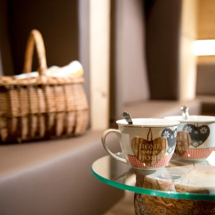 Zwei Keramiktassen mit Herzmotiven und Löffeln auf Glastisch in gemütlicher Lounge mit Picknickkorb
