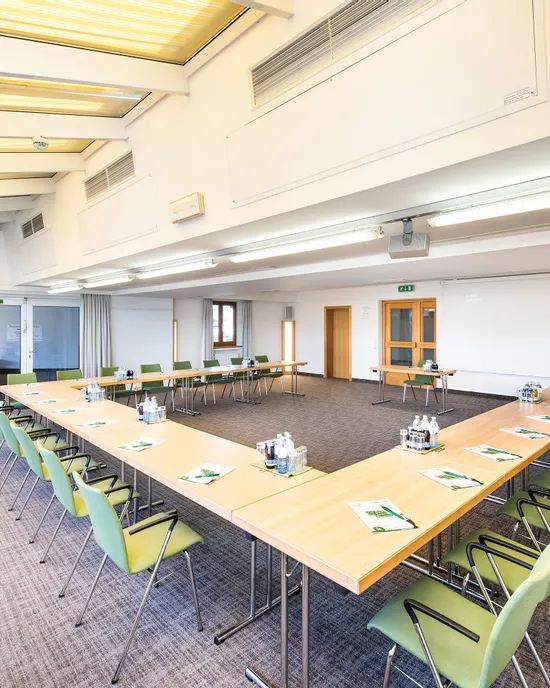 Heller moderner Konferenzraum mit U-förmiger Tischanordnung, grünen Stühlen und Mineralwasser