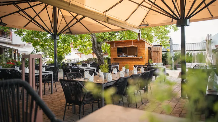 Restaurantterrasse im Freien mit gedeckten Tischen unter großen Sonnenschirmen und viel Grün