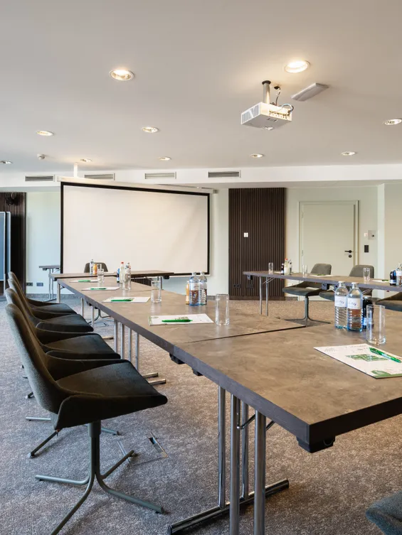 Moderner Konferenzraum mit U-förmigem Tischaufbau, Beamer, Flipcharts und natürlichem Licht