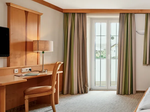 Geräumiges Hotelzimmer mit Doppelbett, Holzmöbeln, Schreibtisch und Tageslicht vom Balkon