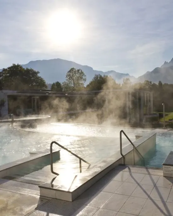 Dampf steigt aus einem Außen-Thermalbecken mit Blick auf Berge bei Sonnenaufgang
