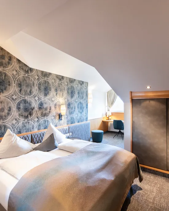 Modernes Hotelzimmer mit Doppelbett, gemusterter Wand, Schreibtisch und Einbauschrank