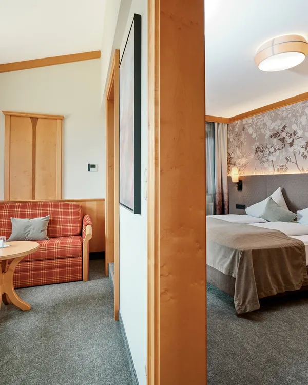 Gemütliches Hotelzimmer mit Doppelbett, karierter Couch und moderner Holzverkleidung