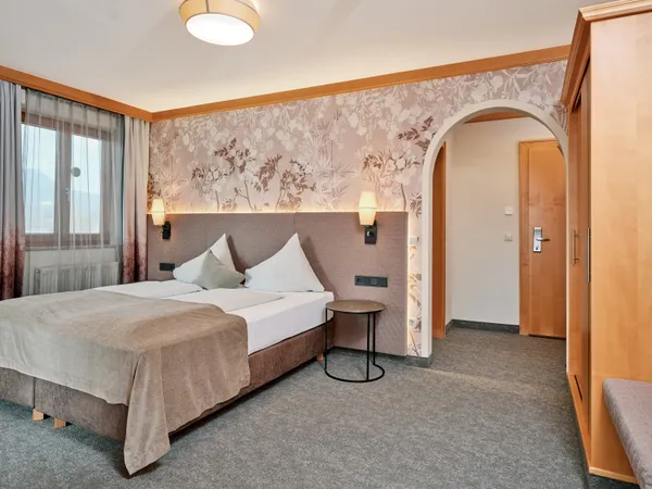 Gemütliches Hotelzimmer mit Doppelbett, Blumenmuster-Tapete und sanfter Beleuchtung