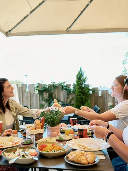 Gruppe von Frauen genießt Frühstück im Freien mit Gebäck, Käse und Kaffee