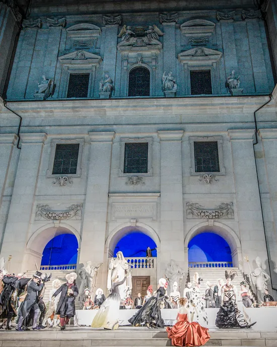Outdoor opera performance with baroque costumes in front of historic stone building at night