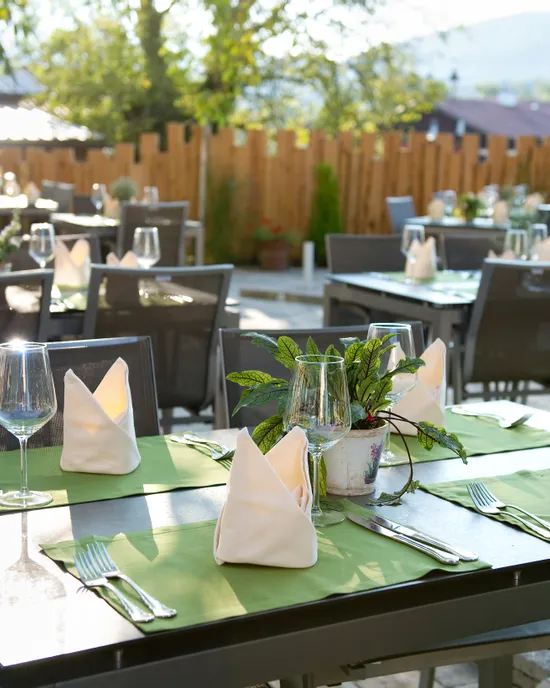 Outdoor restaurant patio with neatly set tables, green placemats, and glassware in sunlight