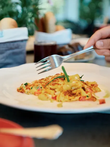 Hand holding fork over fresh vegetable omelette on white plate at breakfast table