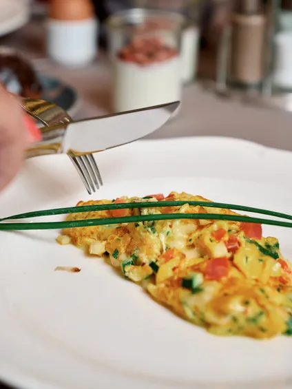 Omelette di verdure guarnita con erba cipollina su piatto bianco tagliata con forchetta e coltello