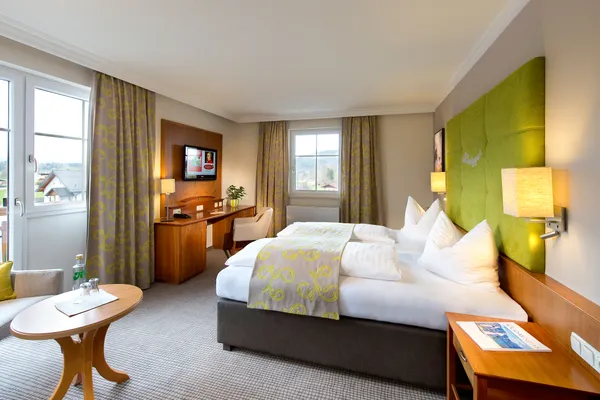 Modernes Hotelzimmer mit Doppelbett, grünem Kopfteil, Schreibtisch und Bergblick