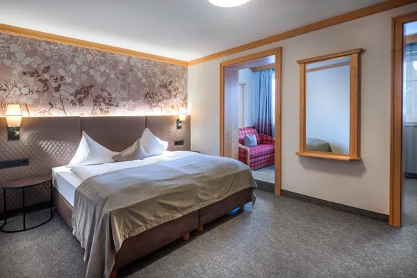 Accogliente camera d'hotel con letto matrimoniale, testiera floreale, applique e zona salotto adiacente
