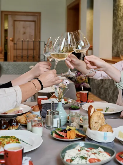 Vier Frauen stoßen beim gemütlichen Frühstück mit Weißwein an