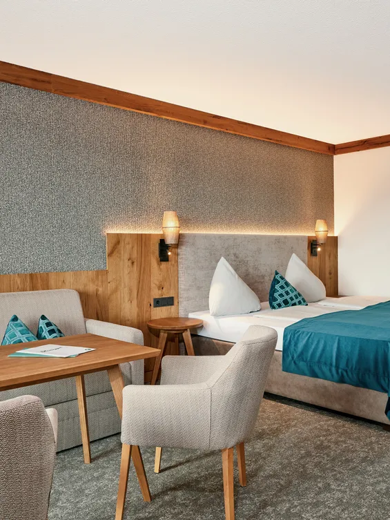 Modernes Hotelzimmer mit Doppelbett, Sofa, Holztisch und türkisfarbenen Akzenten