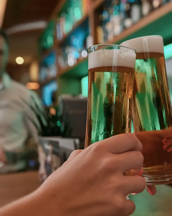 Zwei Personen stoßen mit Stiegl-Biergläsern an der Bartheke an