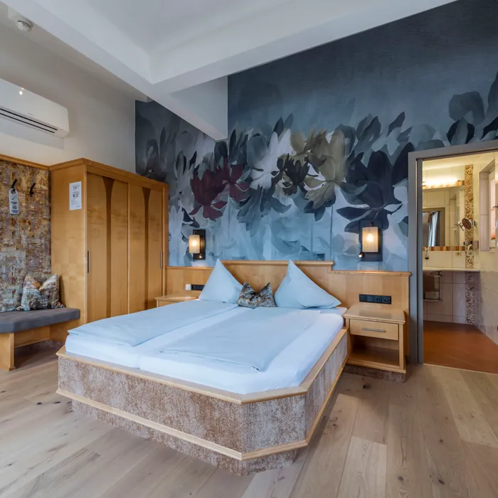 Hotelzimmer mit moderner Einrichtung, Holzboden, großem Bett, Blumenwandbild und eigenem Bad