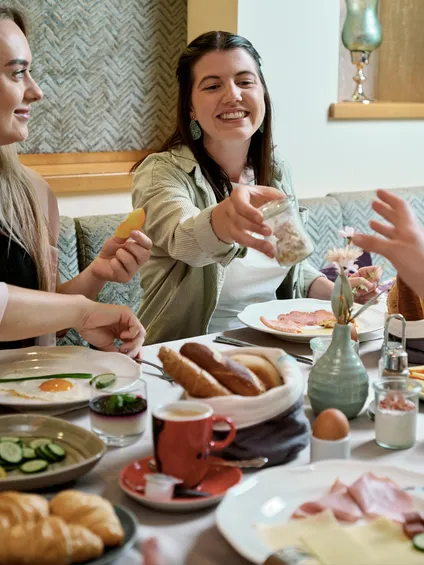Freunde genießen gemeinsam Frühstück mit Eiern, Aufschnitt, Croissants und Kaffee