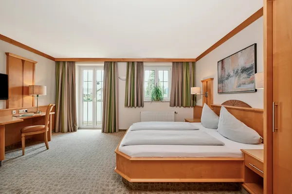Geräumiges Hotelzimmer mit Doppelbett, Holzmöbeln, Schreibtisch und Tageslicht vom Balkon