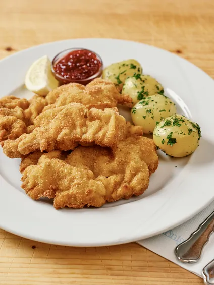 Cotoletta alla viennese croccante con patate al prezzemolo, fette di limone e salsa ai mirtilli rossi