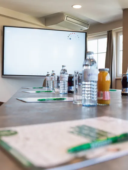 Modern conference room setup with drinks, notepads, and large presentation screen