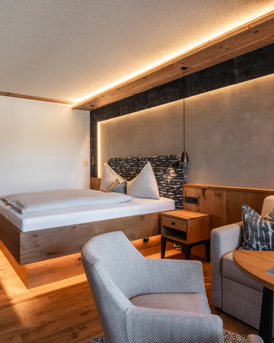 Modernes Hotelzimmer mit Holzmöbeln, gemütlichem Bett, Sofa, Sessel und stimmungsvoller Beleuchtung