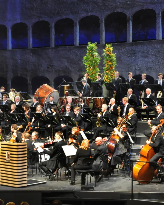 Symphonieorchester in festlicher Kleidung mit Streichern, Bläsern und Schlagzeug auf der Bühne