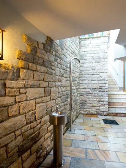 Stone-tiled spa area with wall-mounted lights, metal shower, and stairs leading up