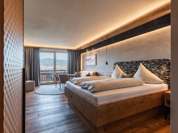 Modernes Alpenhotelzimmer mit Holzmöbeln, Doppelbett und Balkon mit Bergblick