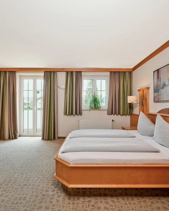 Geräumiges Hotelzimmer mit Doppelbett, Holzmöbeln, Schreibtisch und Tageslicht vom Balkon