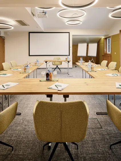 Modern conference room with U-shaped wooden table, beige chairs, and presentation equipment