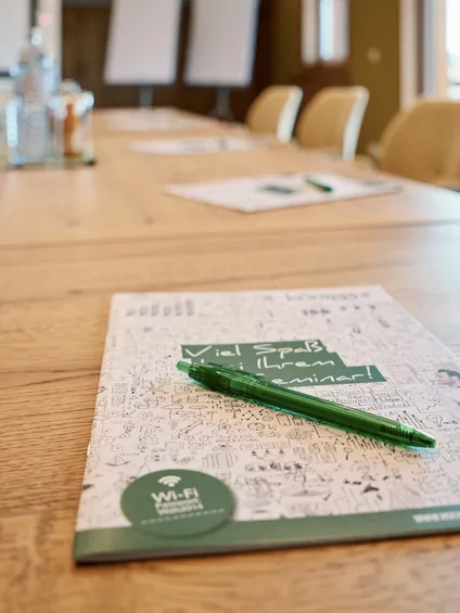 Seminarblock und grüner Stift auf Konferenztisch im modernen Tagungsraum