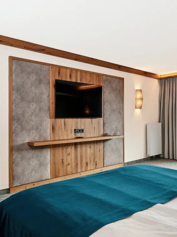 Modernes Hotelzimmer mit Doppelbett, TV-Wand aus Holz und Zugang zum Balkon