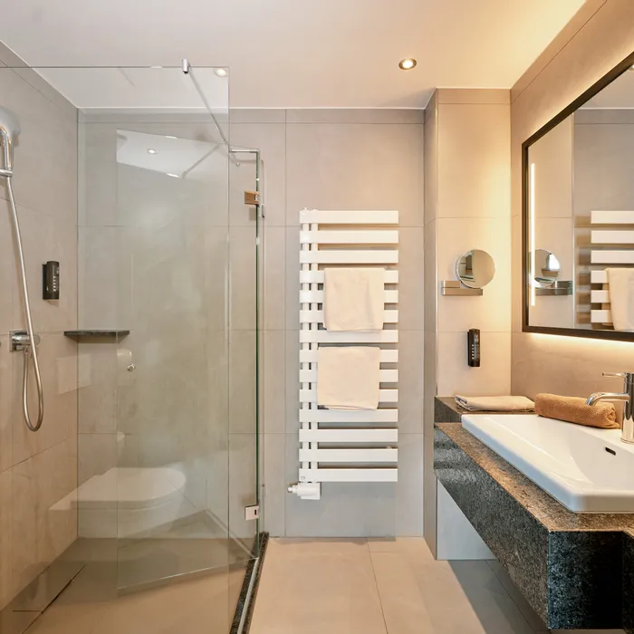 Modernes Hotelbad mit begehbarer Dusche, großem Spiegel und Waschbecken mit Granitplatte