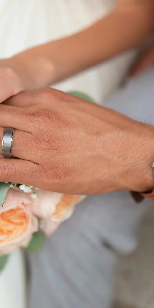 Mani di sposi con fedi nuziali poggiate su un bouquet di rose pesca