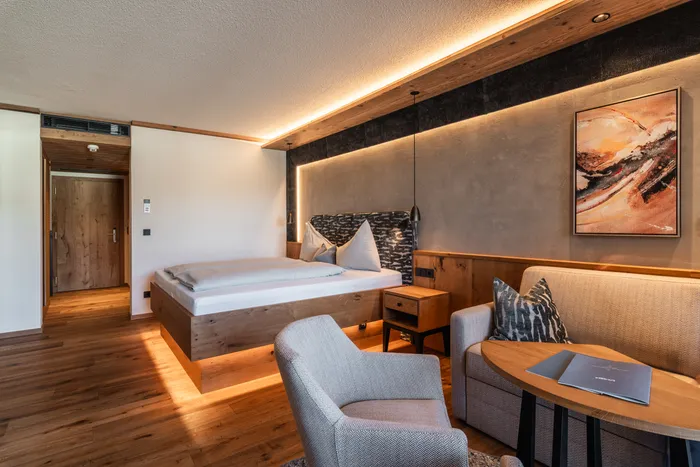 Modern hotel room with wooden furnishings, cozy bed, sofa, armchair and ambient lighting
